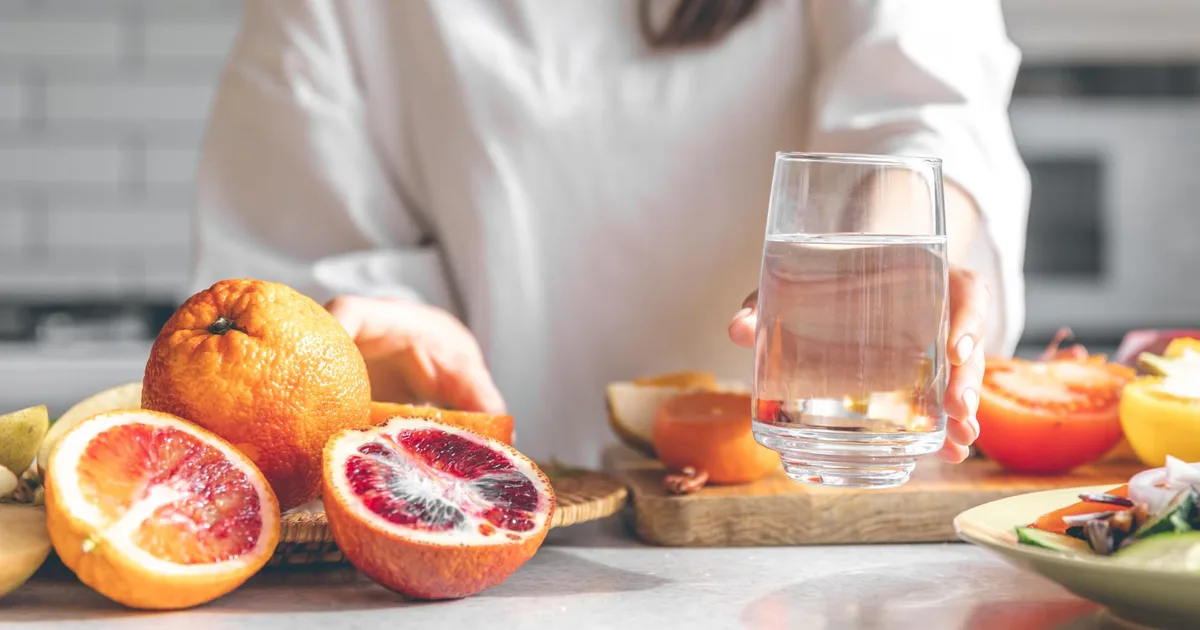 Vaso de agua y fruta fresca sobre una mesa de cocina con luz natural