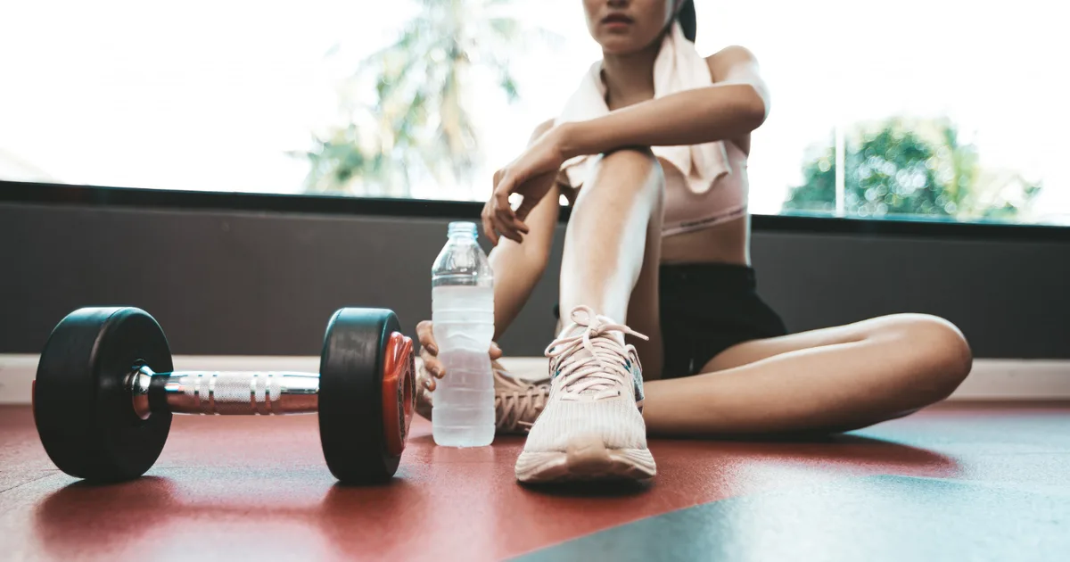 Persona entrenando con mancuernas en casa junto a unas zapatillas de correr