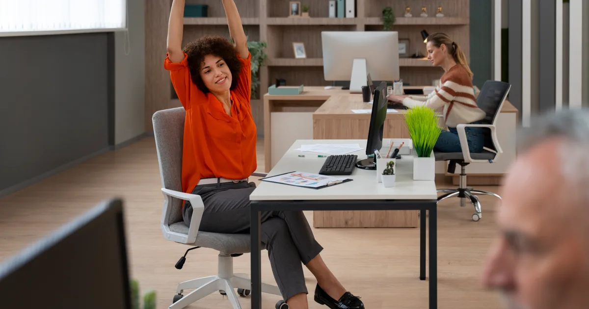 Mujer estirando los brazos junto a su escritorio durante una pausa en la jornada laboral