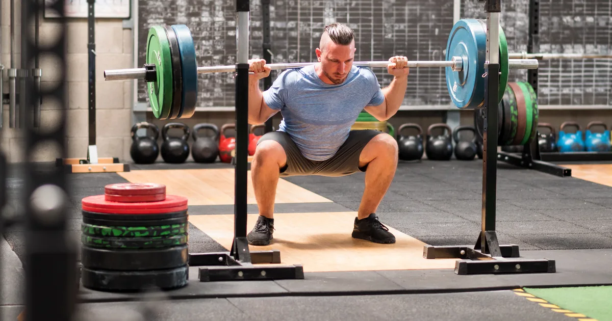 Athlete performing a barbell back squat in the gym, seen from the side, with good back posture
