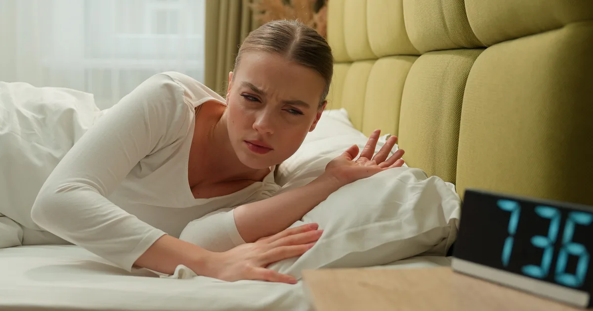 Persona recién despertada, con cara de sueño, sentada en la cama por la mañana temprano