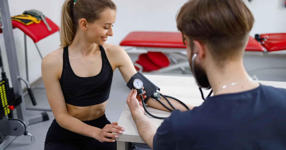 Deportista con ropa de entrenamiento durante una prueba de esfuerzo con una cardióloga en consulta
