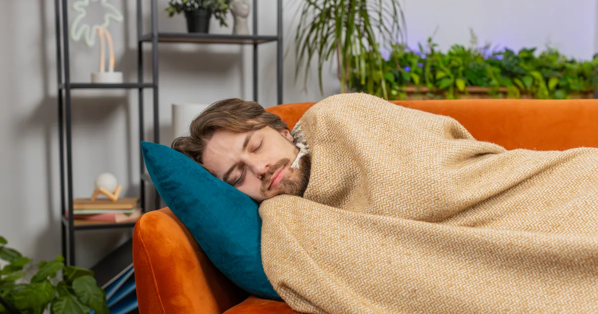 Persona joven durmiendo una siesta en el sofá del salón con luz de día
