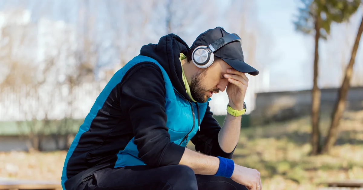 Corredor cansado y pensativo apoyado en un muro de un parque tras un entrenamiento