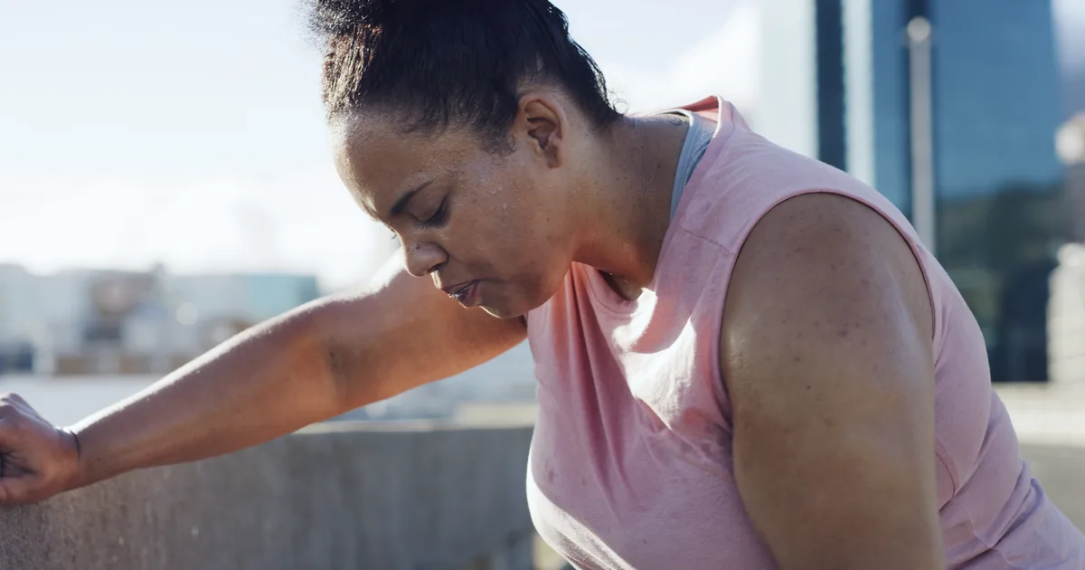 Woman in sportswear sitting outdoors, exhausted after training