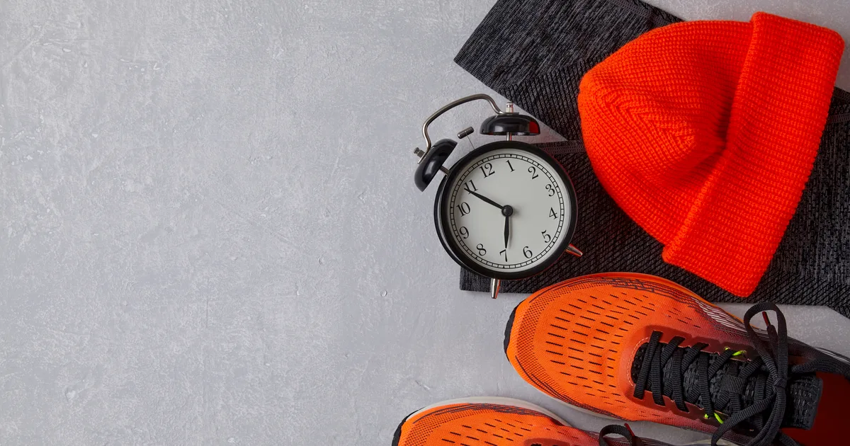 Alarm clock beside orange running shoes and a knitted beanie on a grey background