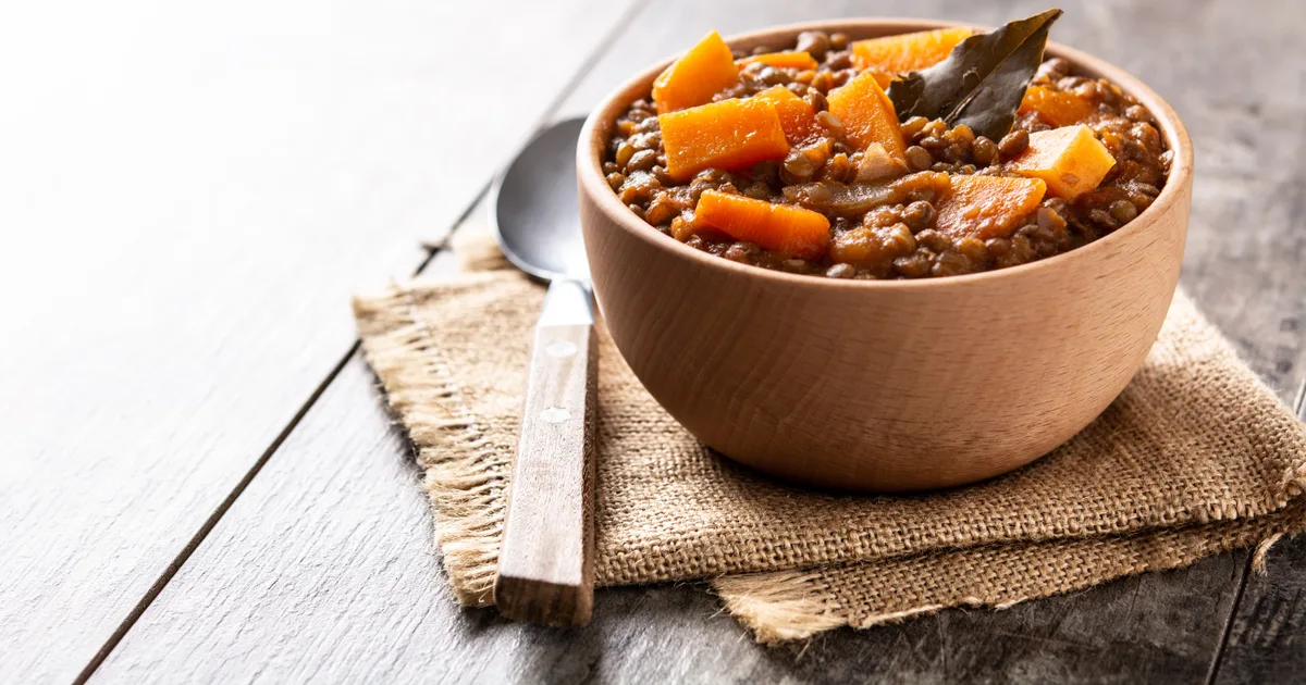 Wooden bowl of lentil stew with pumpkin and carrot on a wooden table