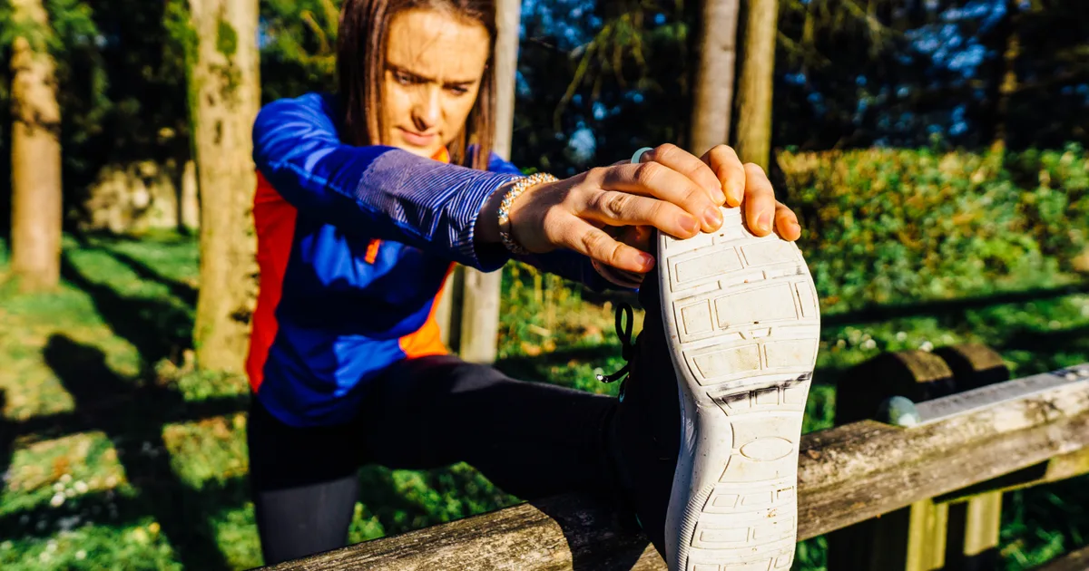 Woman stretching her hamstrings with her foot on a wooden fence in a park