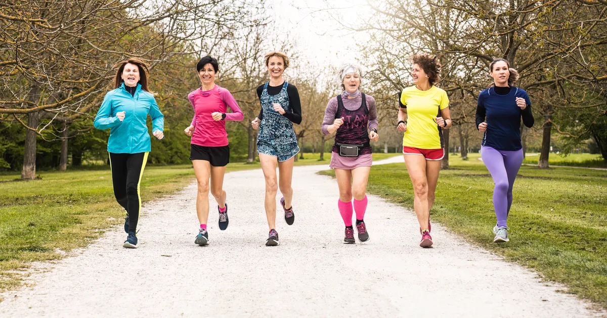 Group of six women of different ages running together and smiling along a park path